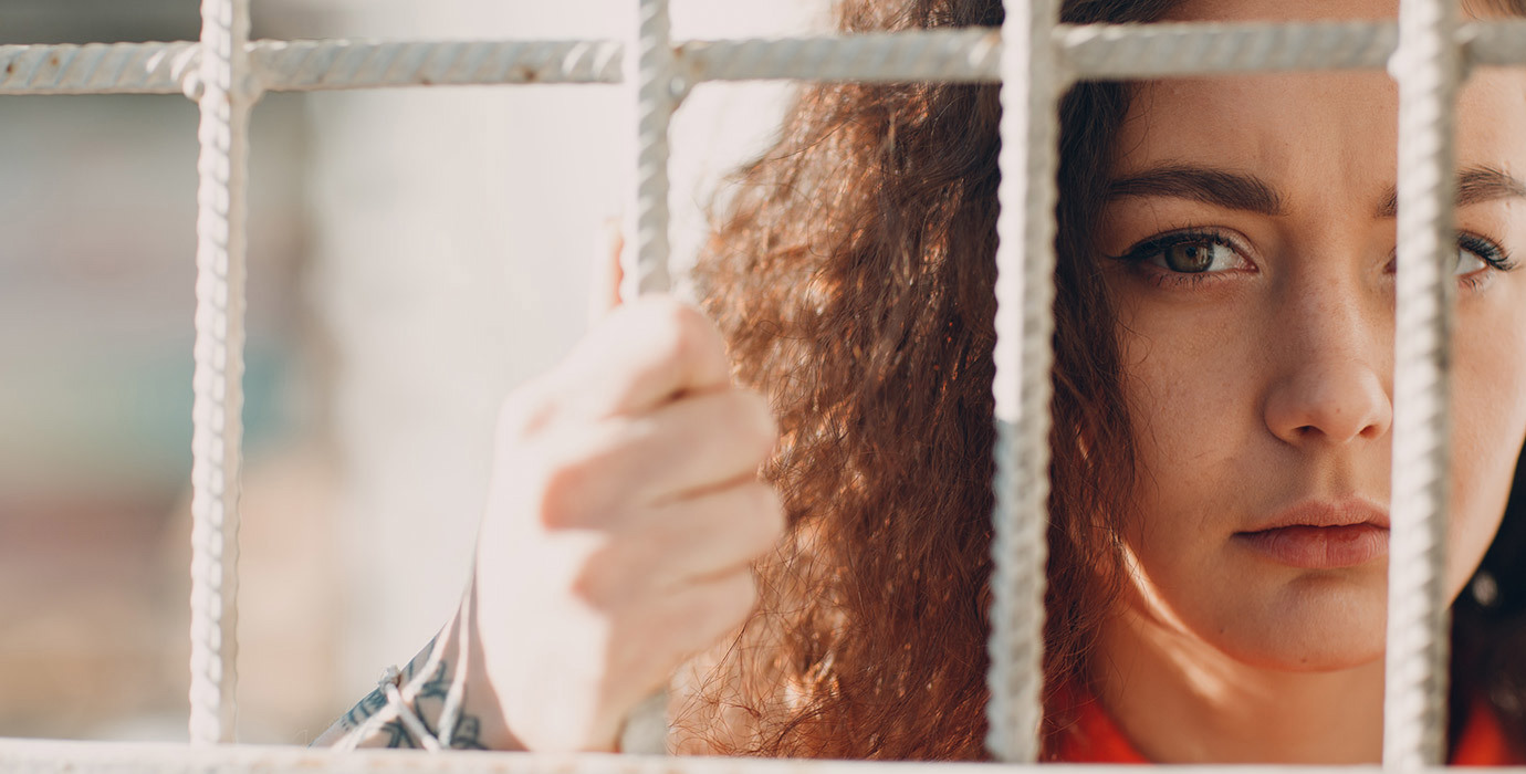 A person looking through bars and holding onto the barrier.