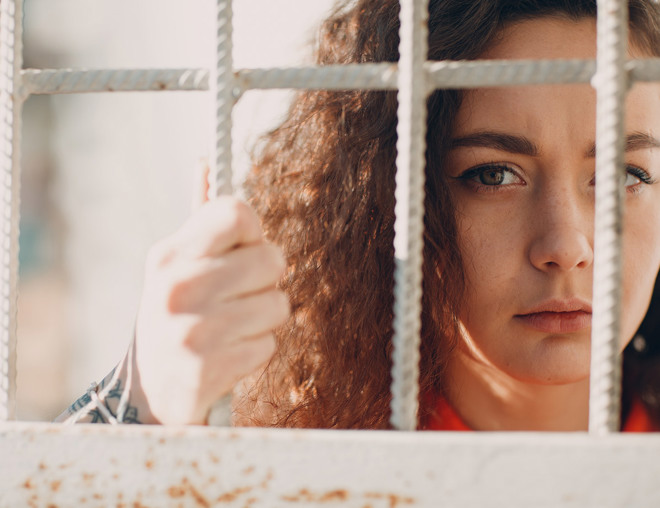 A person looking through bars and holding onto the barrier.