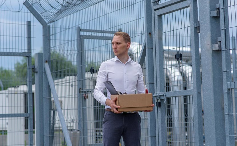 A person carrying a box of personal items standing outside a grey prison fence.