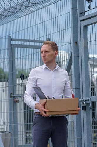 A person carrying a box of personal items standing outside a grey prison fence.