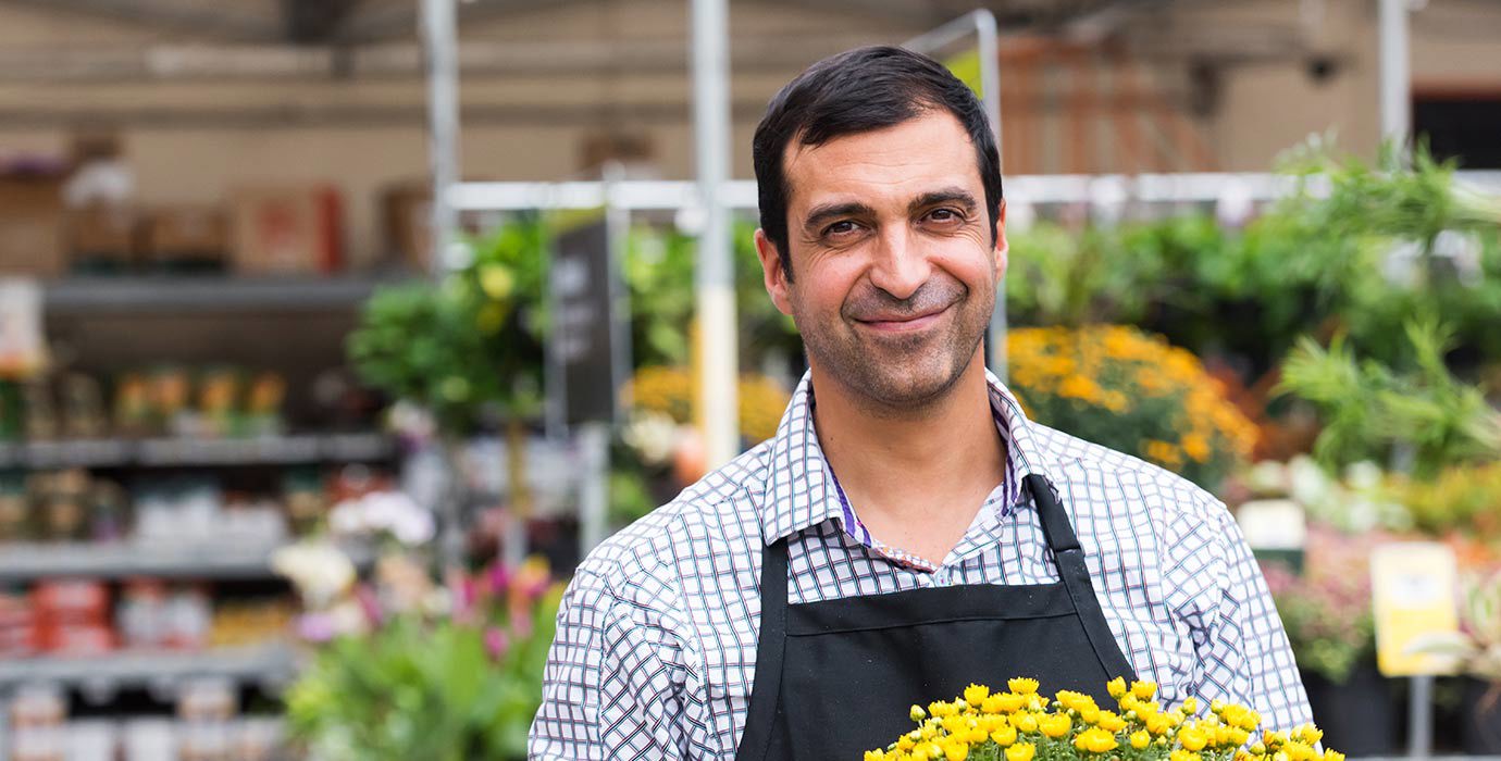 A smiling worker carries a potted plant in a garden centre.