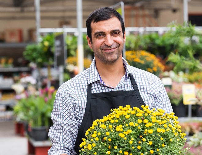 A smiling worker carries a potted plant in a garden centre.