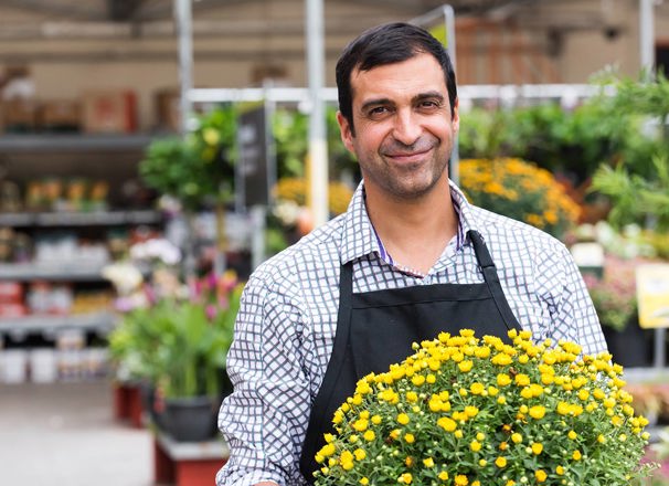 A smiling worker carries a potted plant in a garden centre.