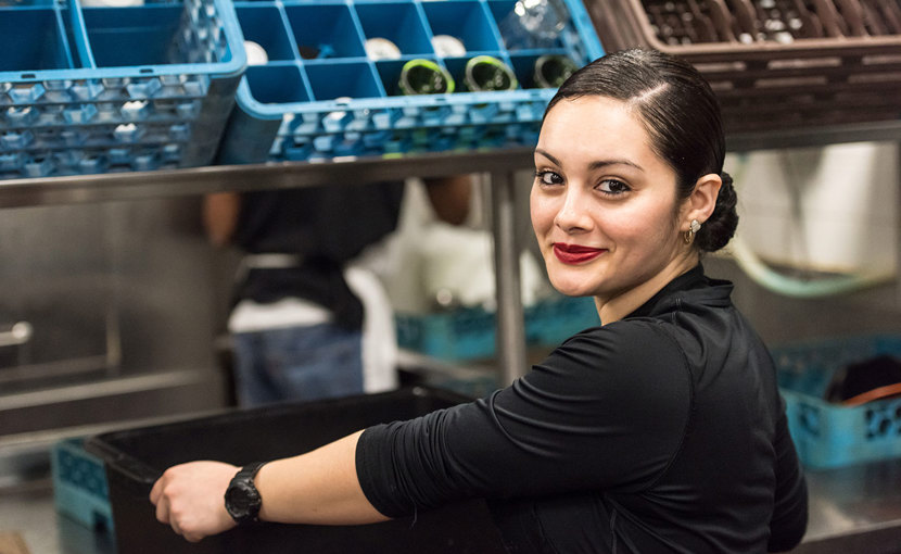 A worker puts a bin of dirty dishes on the counter in a restaurant kitchen.