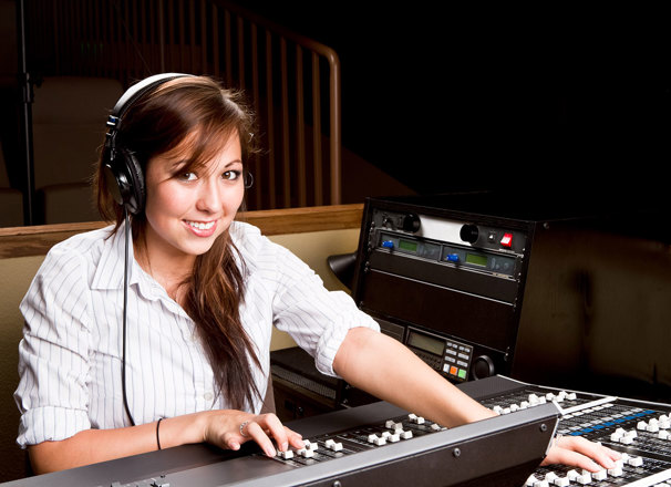 A person wearing headphones sits in front of a mixing console while smiling.