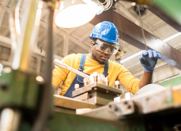 Factory engineer in hardhat and overalls using a lathe.