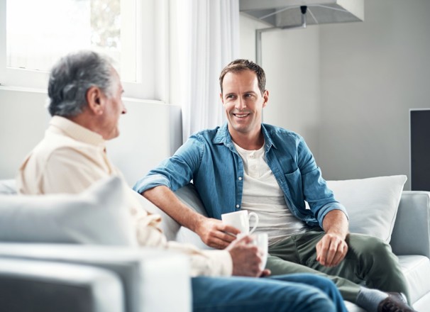 Father and son talking while sitting on couch and drinking coffee.