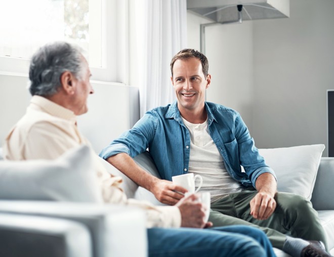 Father and son talking while sitting on couch and drinking coffee.