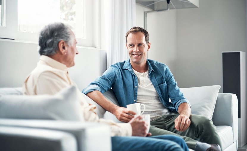 Father and son talking while sitting on couch and drinking coffee.