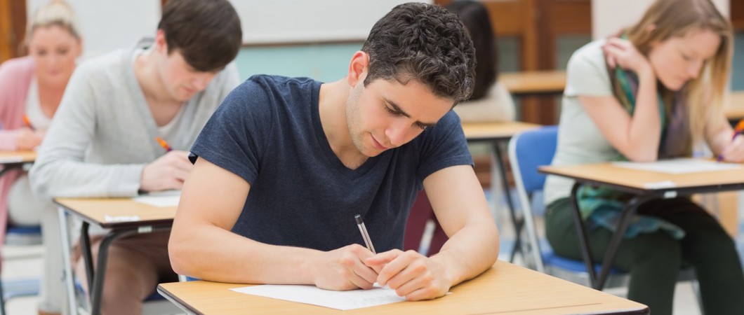 Post-secondary student writing exam at desk in a classroom.