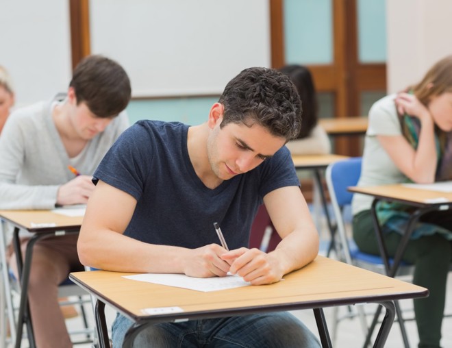 Post-secondary student writing exam at desk in a classroom.