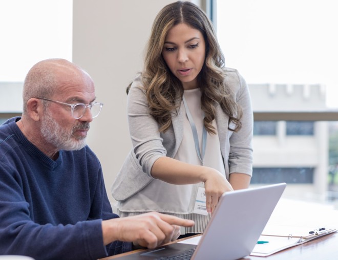 Teacher helps a mature student with using software on a laptop computer.