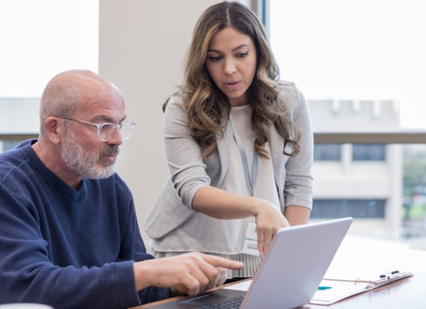 Teacher helps a mature student with using software on a laptop computer.