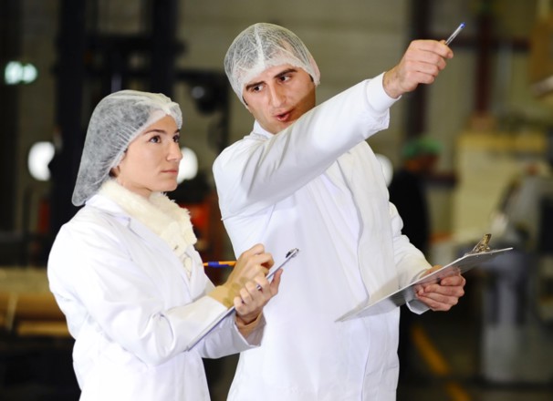 Two workers in hairnets and lab coats inspecting equipment.
