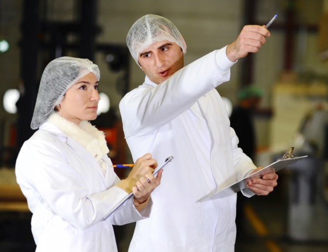 Two workers in hairnets and lab coats inspecting equipment.