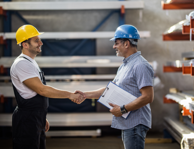 Two workers shaking hands in warehouse.