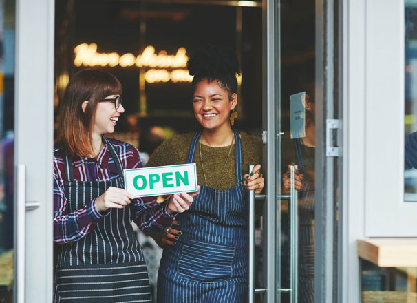 People holding an "Open" sign in front of their cafe