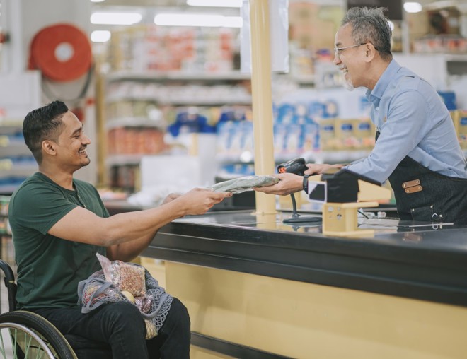 Person in wheelchair paying for groceries at checkout.