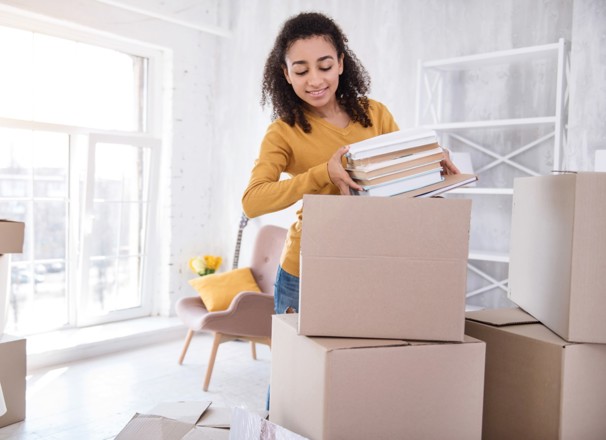 Student unpacking books from boxes in dorm room.
