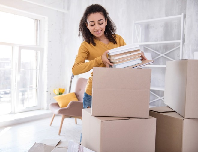 Student unpacking books from boxes in dorm room.