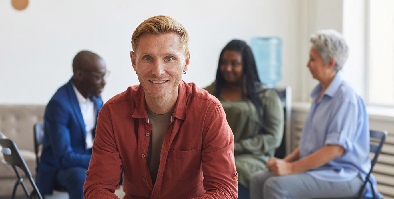 Person smiling at the camera sitting in front of a group session