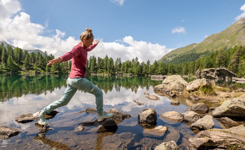 Person walking along rocks in a shallow part of a mountain lake.