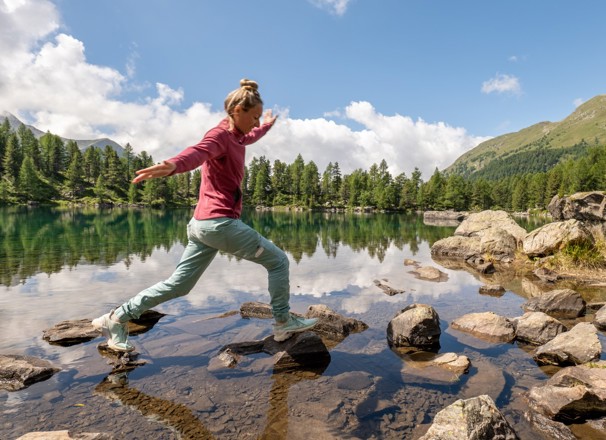 Person walking along rocks in a shallow part of a mountain lake.