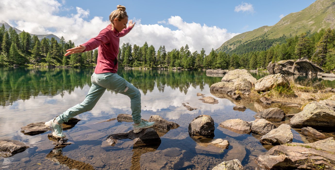 Person walking along rocks in a shallow part of a mountain lake.