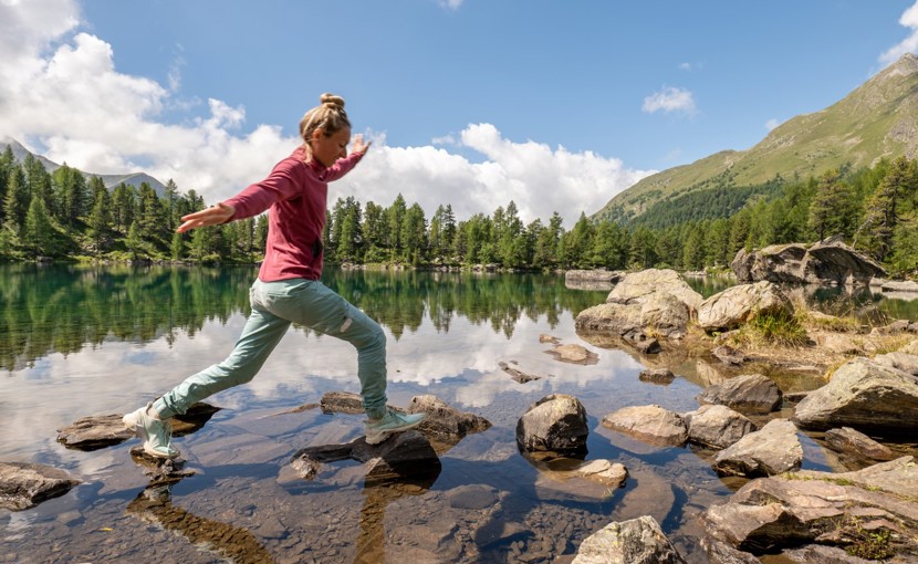 Person walking along rocks in a shallow part of a mountain lake.