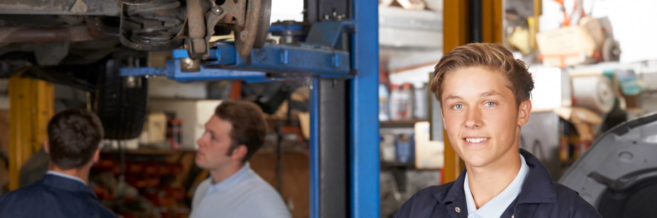 Apprentice holding clipboard while working in a mechanic shop.