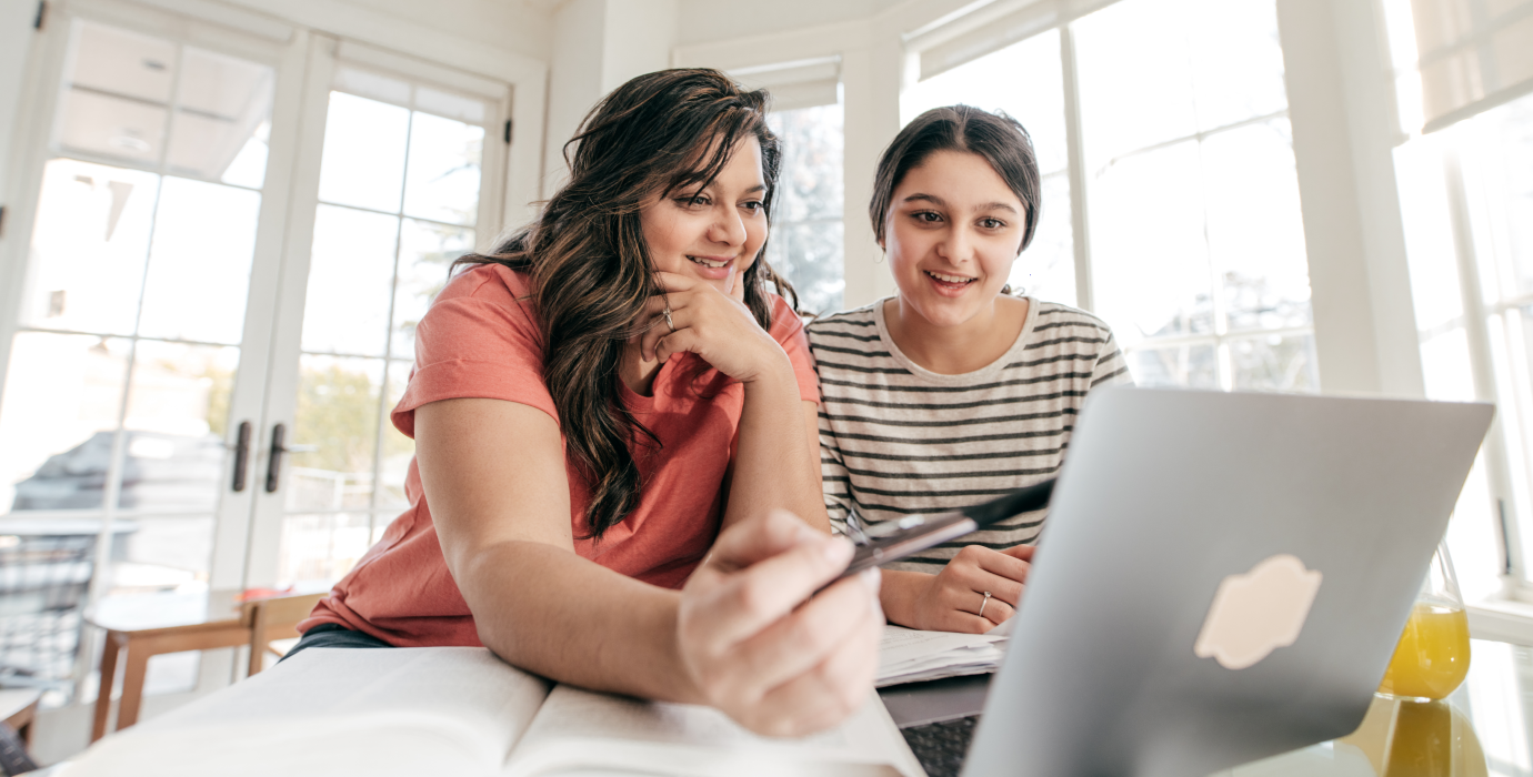 Mother pointing at laptop screen while daughter watches.