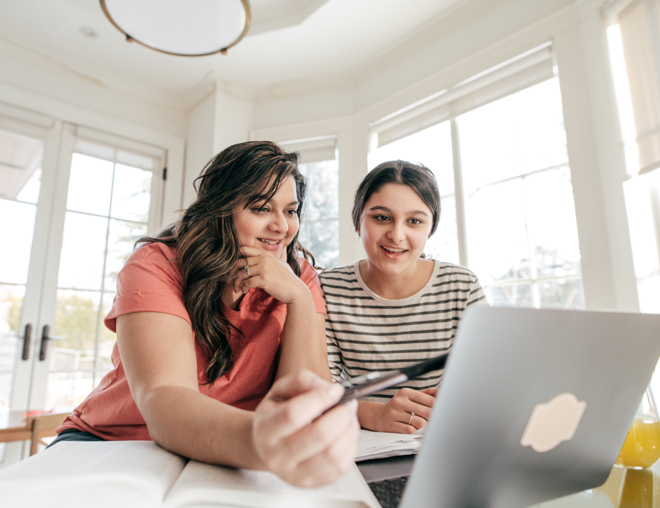 Mother pointing at laptop screen while daughter watches.