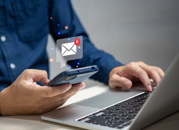 person emailing with a cellphone and a laptop