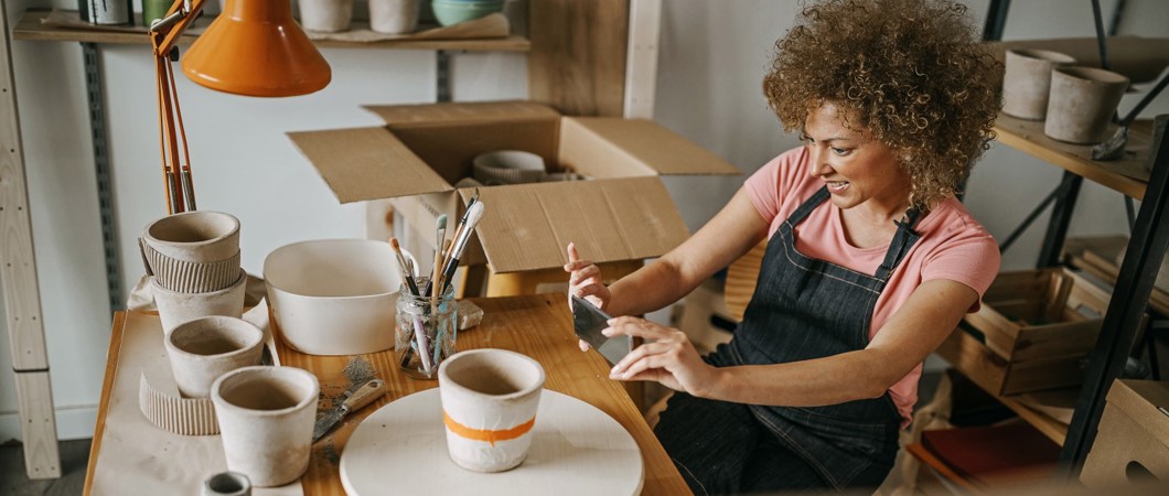 Woman wearing a denim apron taking a picture of a clay pot she painted