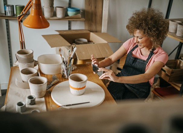 Woman wearing a denim apron taking a picture of a clay pot she painted