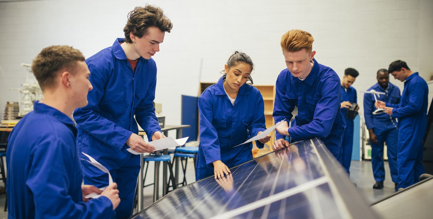 Four students look over a solar panel and make notes.