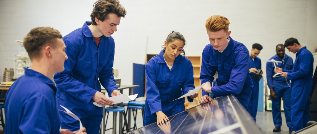 Four students look over a solar panel and make notes.