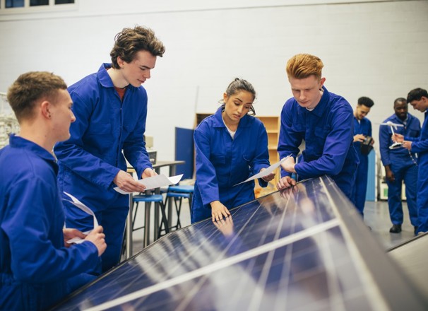 Four students look over a solar panel and make notes.