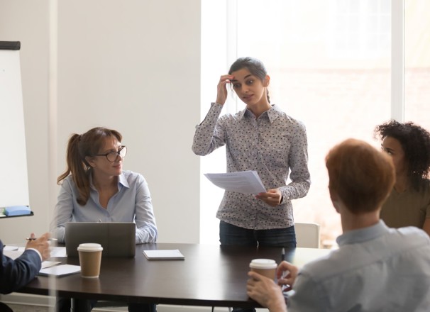 Presenter looks nervous as she speaks to a table of coworkers.