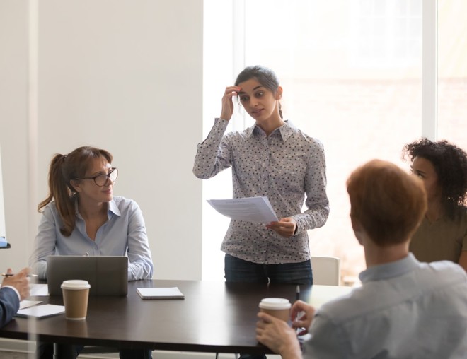 Presenter looks nervous as she speaks to a table of coworkers.