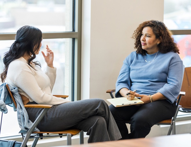 Two people talking at a table by a window. 