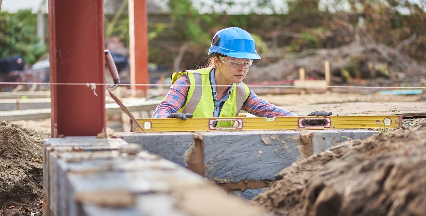 Apprentice bricklayer using a level to check a row of bricks.