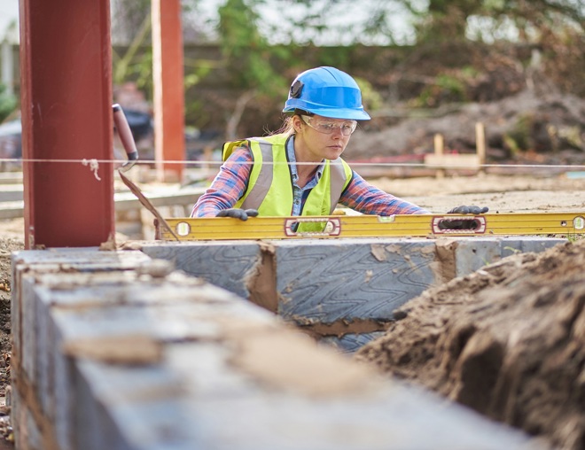 Apprentice bricklayer using a level to check a row of bricks.