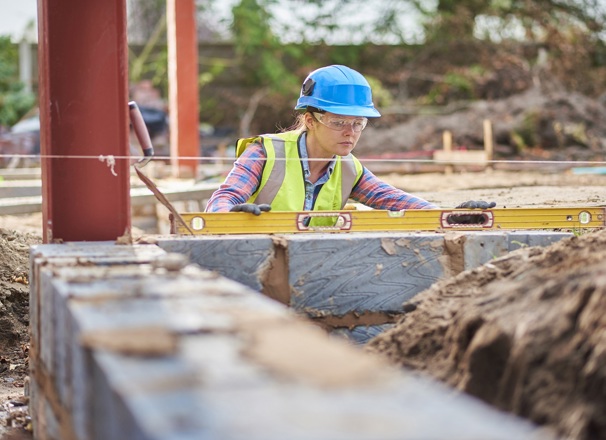 Apprentice bricklayer using a level to check a row of bricks.