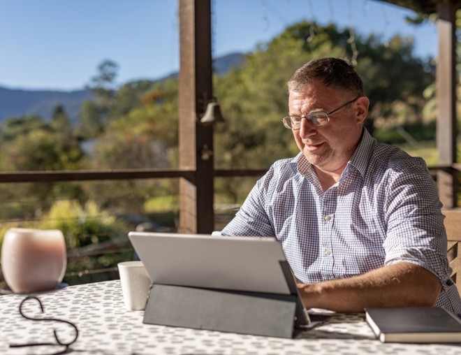 Person working on laptop on their porch in a rural setting.