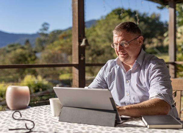 Person working on laptop on their porch in a rural setting.