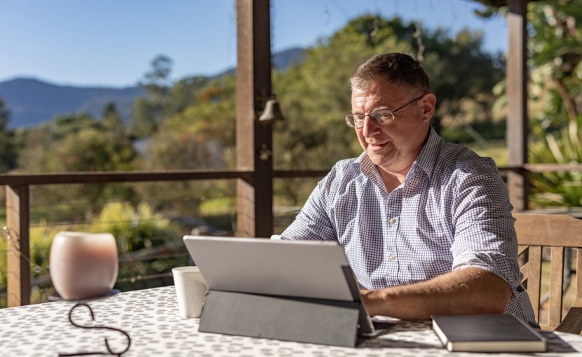 Person working on laptop on their porch in a rural setting.