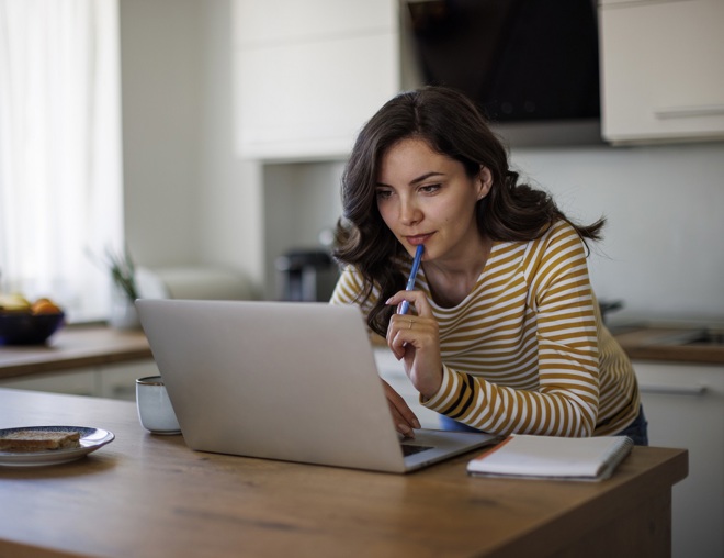 Person using laptop while standing over kitchen counter. 