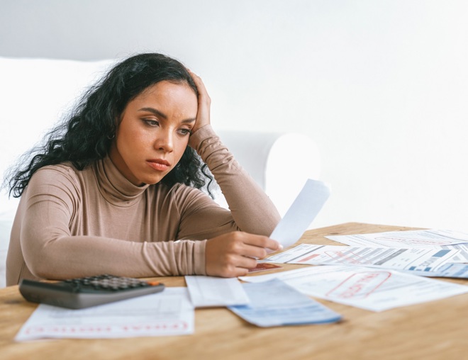 Person looking stressed while looking over a table of bills and receipts.