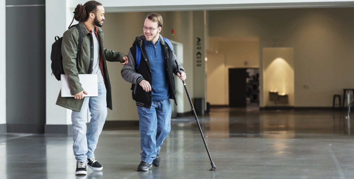 Person walking with a disabled student in school hallway. 